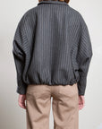 Pharaoh’s Andre Bomber Jacket in wool pinstripe, tan pants, back view; minimalist setting with plain wall.