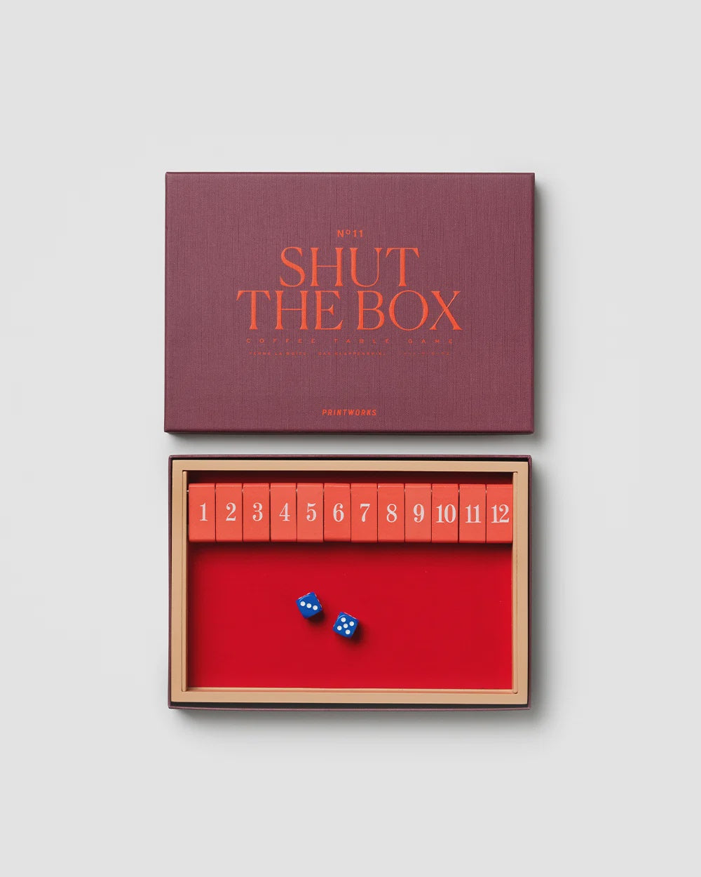 Printworks Shut The Box wooden game with numbered board and two blue dice, shown with its storage box.