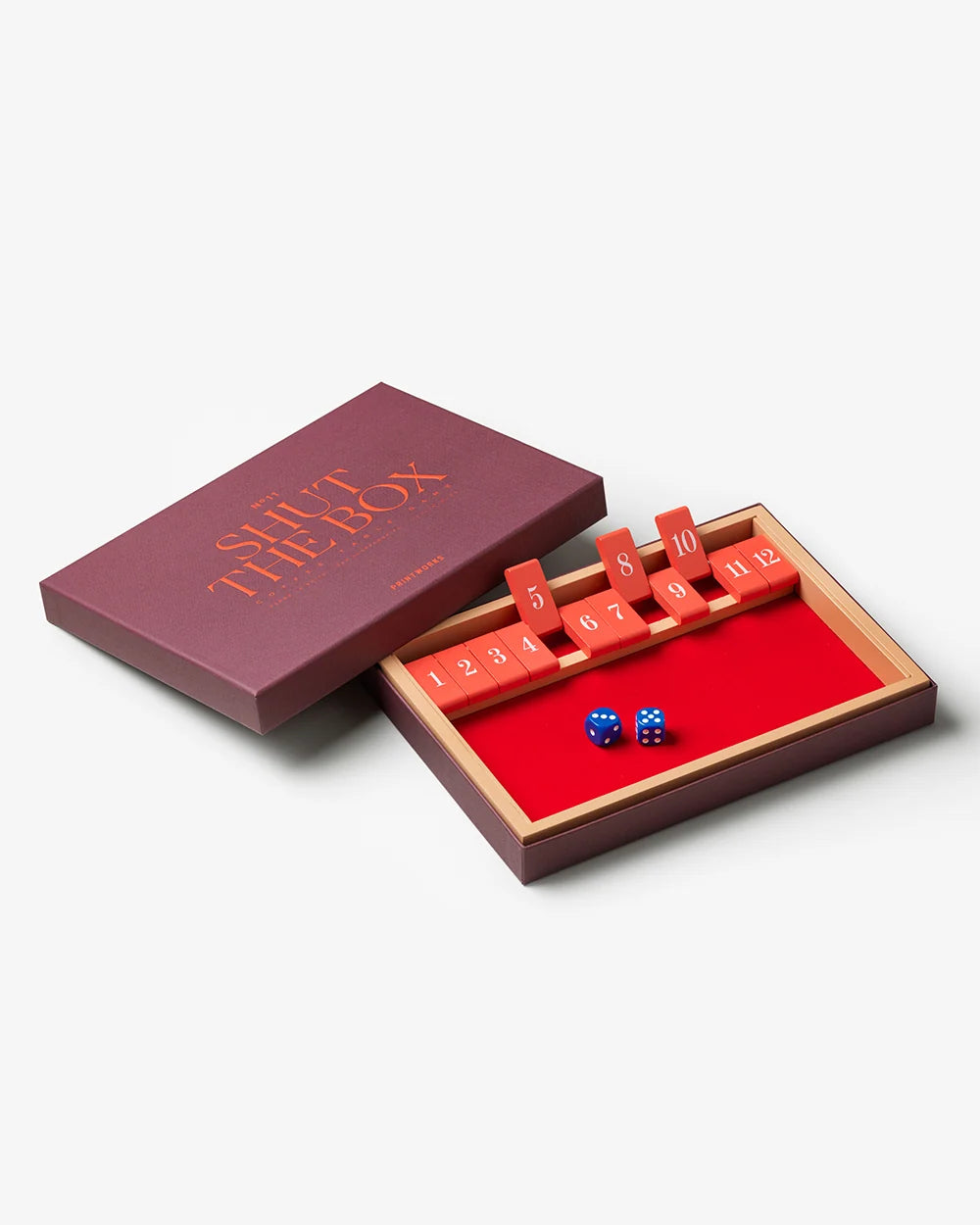 Printworks Shut The Box classic wooden game with red tiles and blue dice beside its purple box lid.