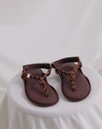 Brown leather Flowze FLO sandals with knotted straps displayed on a white-draped table, Bungalow Furniture.