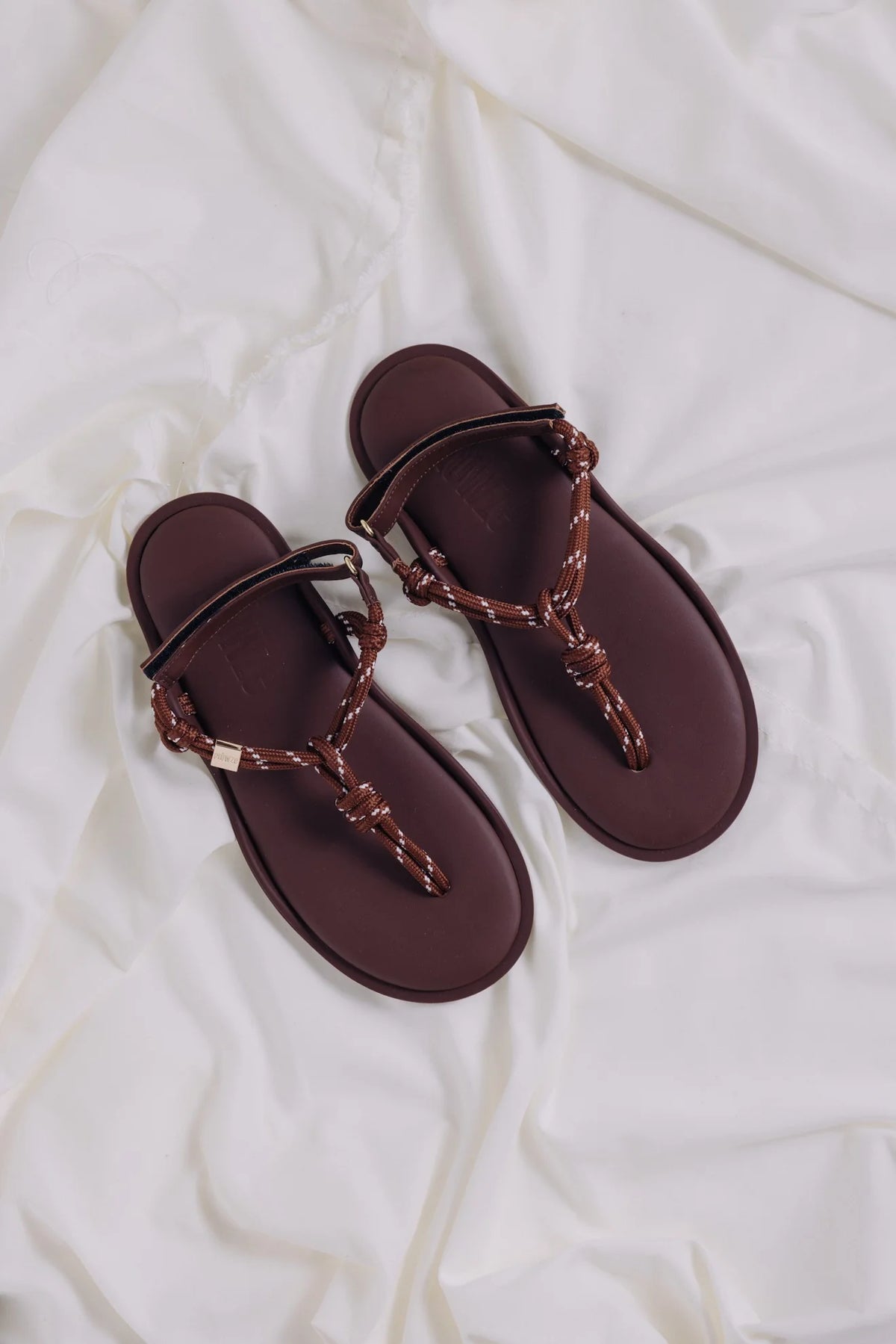 Brown knotted strap sandals by Flowze, FLO style, displayed on a soft white fabric background.