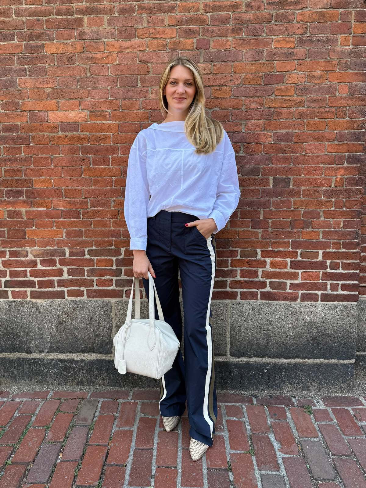 Rachel Comey Dallbey Top in a relaxed style, worn by a smiling woman next to a brick wall with a white bag.