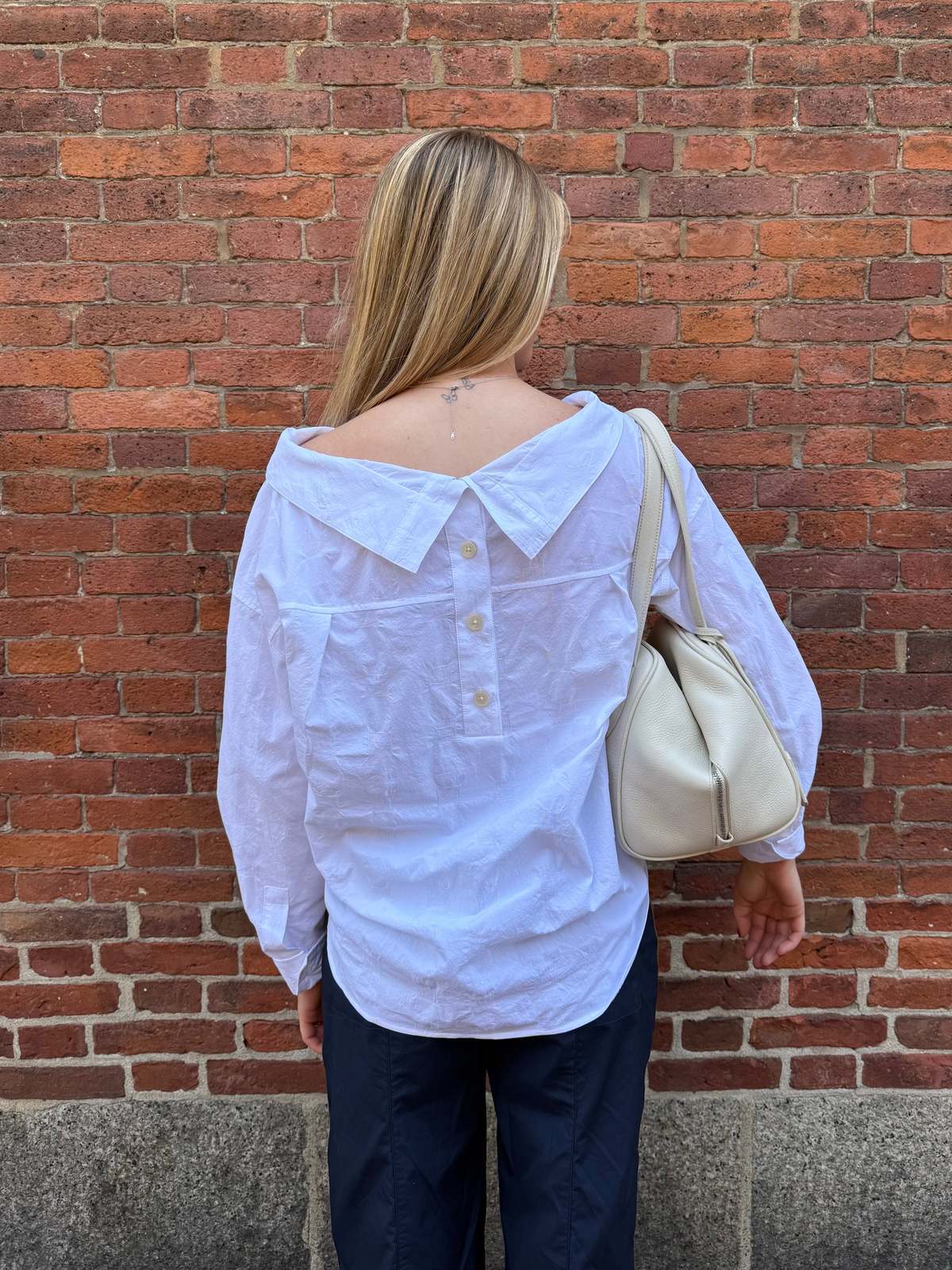 Rachel Comey Dallbey Top in cream, styled with a cream bag by a brick wall for a relaxed, modern look.