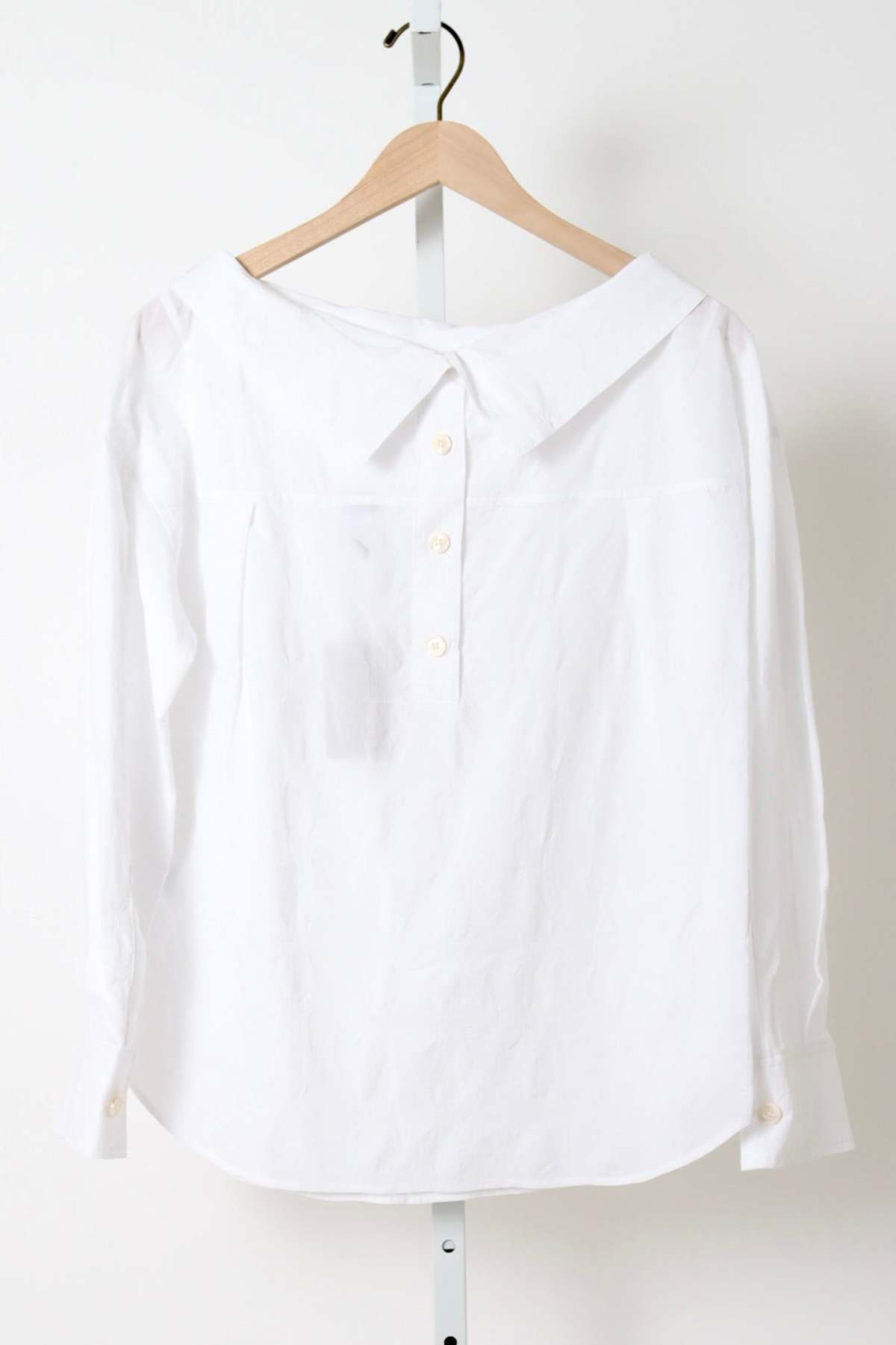 White Rachel Comey Dallbey Top, cotton long-sleeve blouse on wooden hanger, neutral background.
