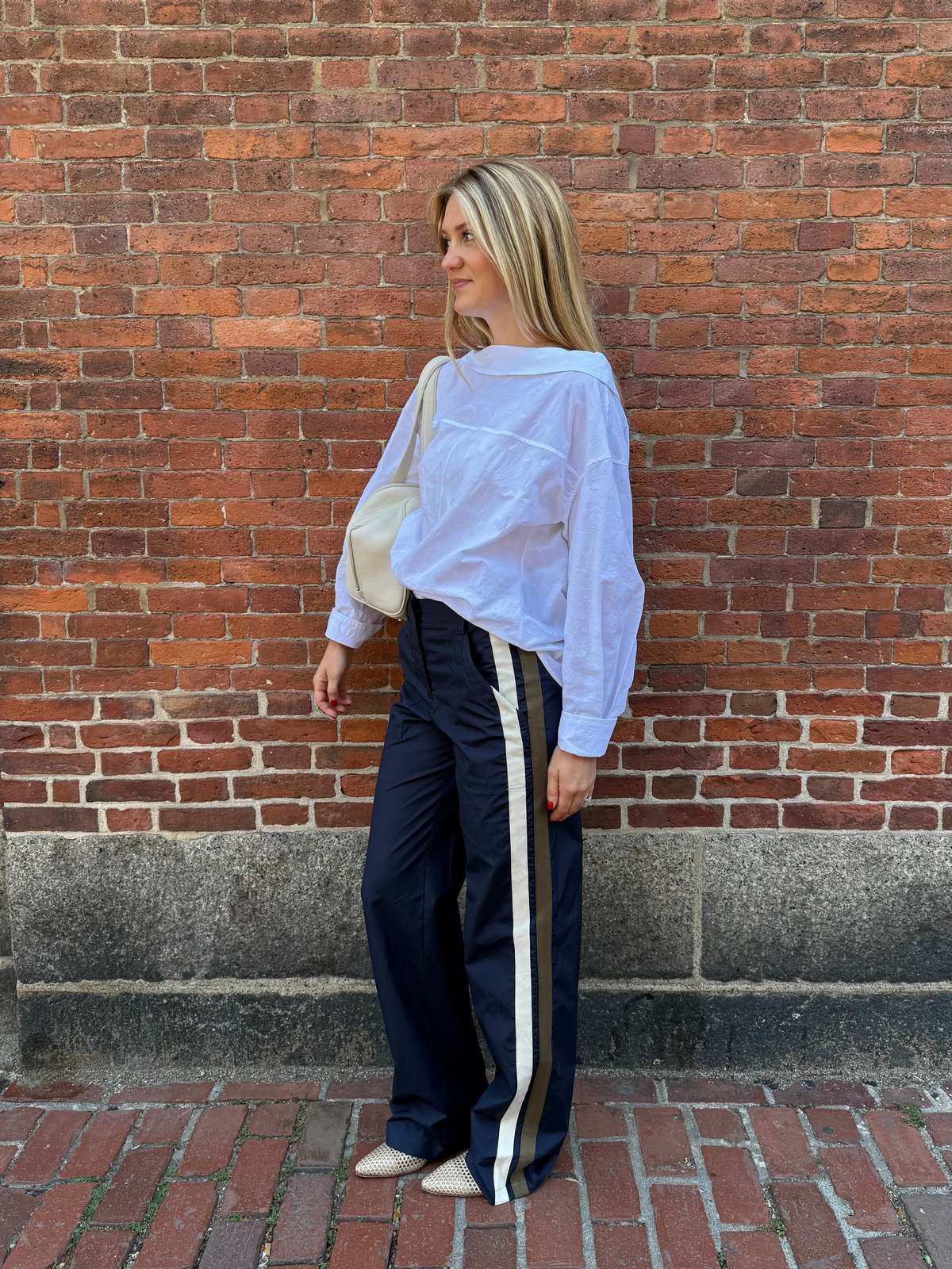 Rachel Comey Dallbey Top in a casual look, styled with navy pants and white bag against a brick wall backdrop.