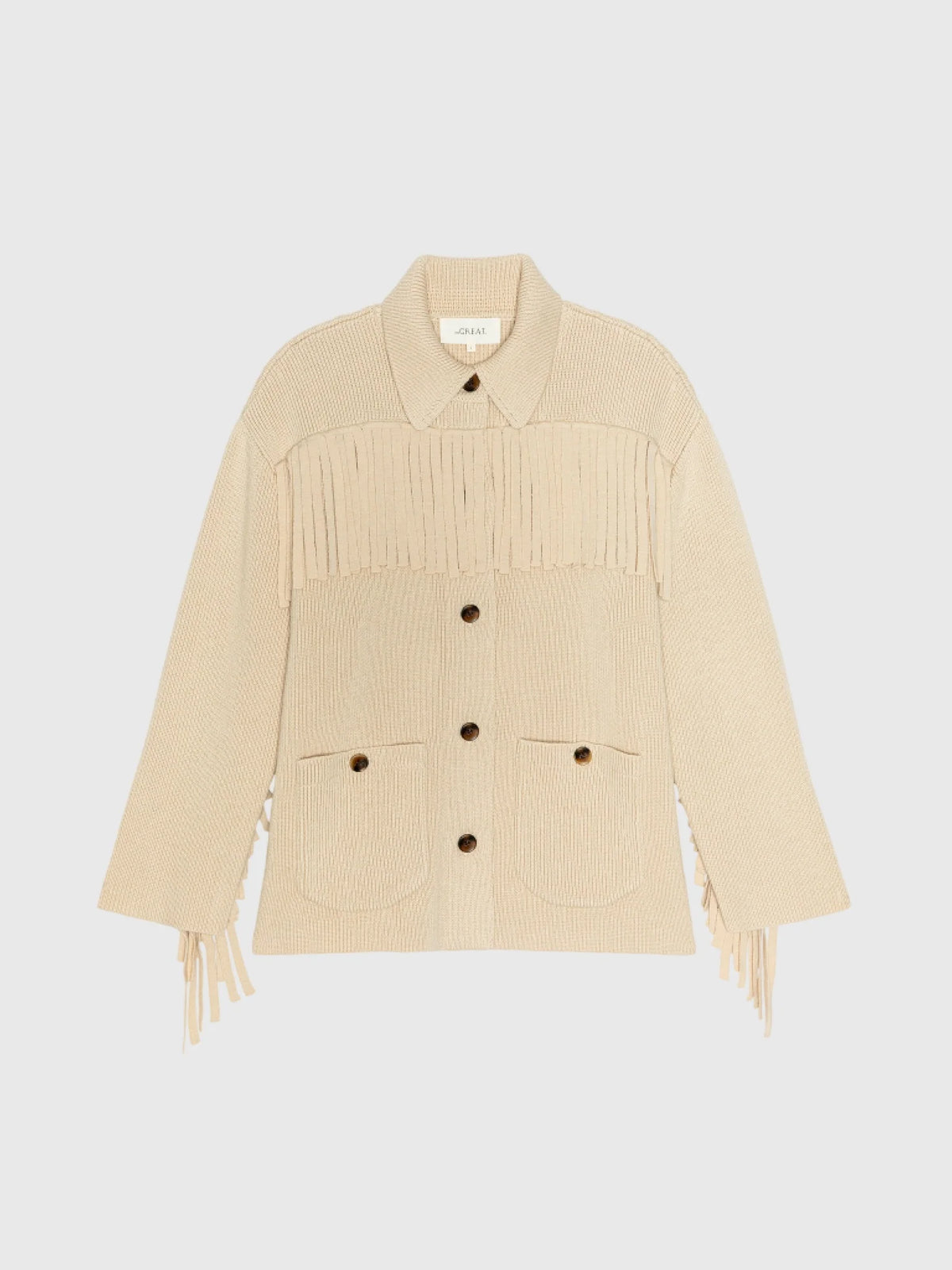 Natural sweater jacket with fringe and front pockets by The Great Inc., Western Fringe style, shown on white background.