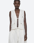 A person faces forward wearing the Sea New York Lois Twill Vest, featuring an oversized utilitarian design with front ties and large pockets, paired with loose white pants against a plain, light-colored background.