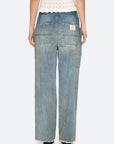 A person wearing Sea New York's Claira Mended Jeans in relaxed fit light blue denim, seen from the back with visible pockets and a patch on one pocket, paired with a cream knitted top.