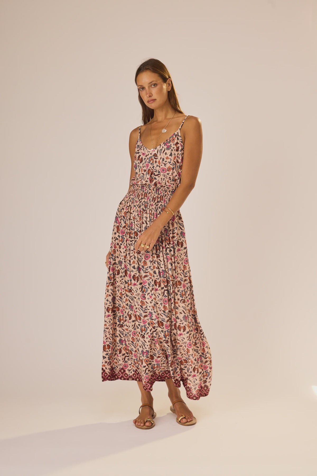 A woman stands against a plain background wearing the natalie martin Bella Skirt, an ankle-length floral rayon skirt with an elastic waist, styled with flat sandals.
