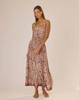 A woman stands against a plain background wearing the natalie martin Bella Skirt, an ankle-length floral rayon skirt with an elastic waist, styled with flat sandals.