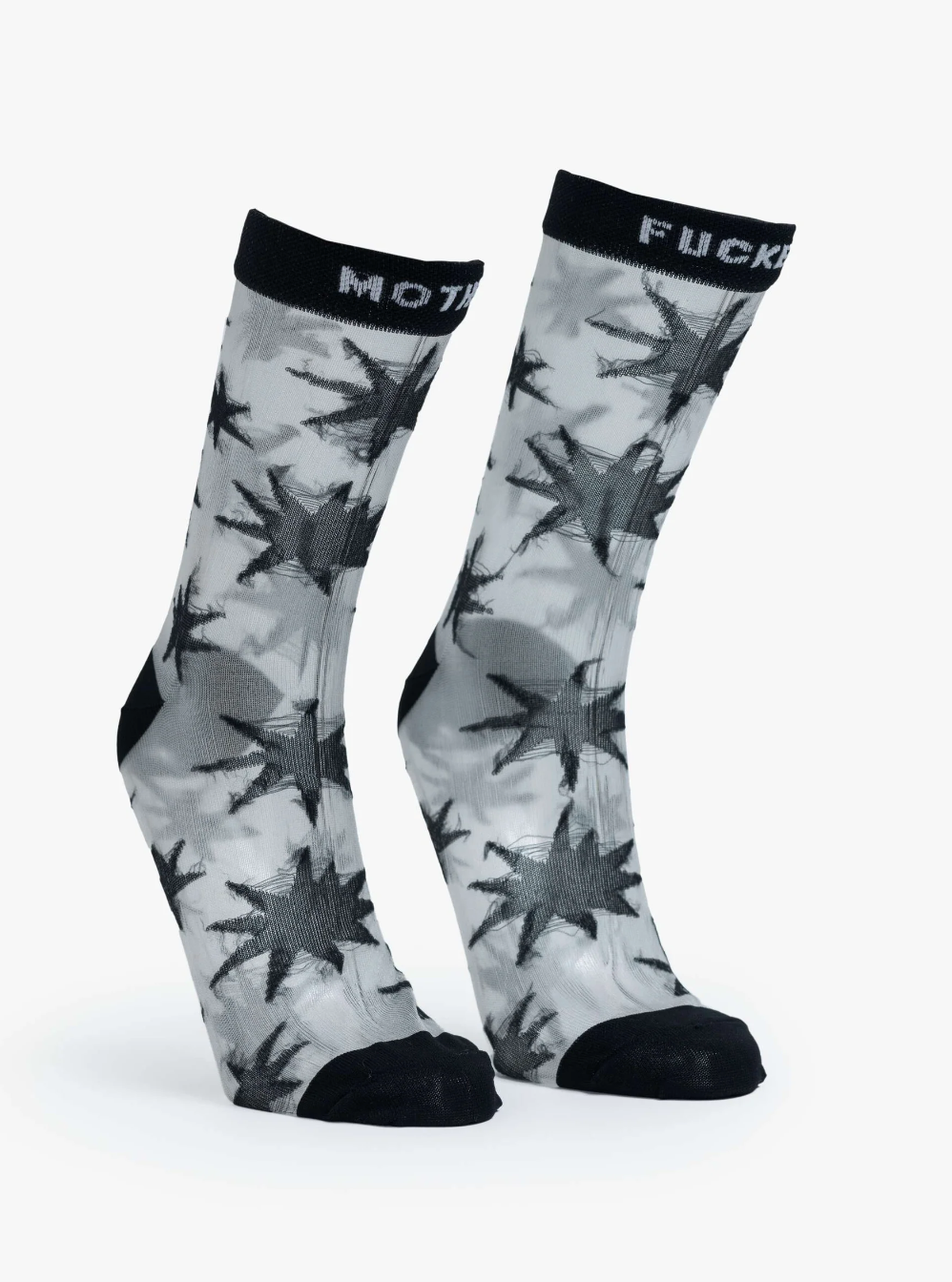 The Step Up Sock by Mother is designed with a translucent grey fabric adorned with bold black star patterns. They feature black tops, each displaying the words "MOT" and "FUCK" in white text. The heel and toe areas are stylishly accentuated in black.