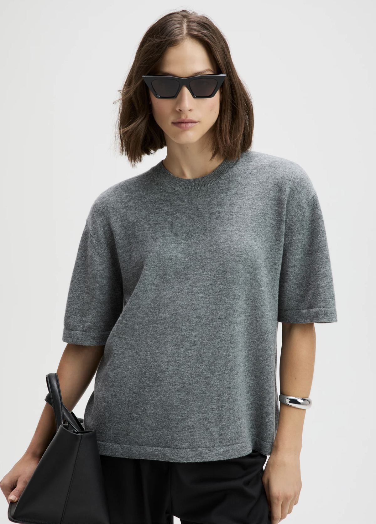 The Cashmere Oversized Tee in soft grey by Sold Out NYC, styled with black bag and sunglasses against light background.