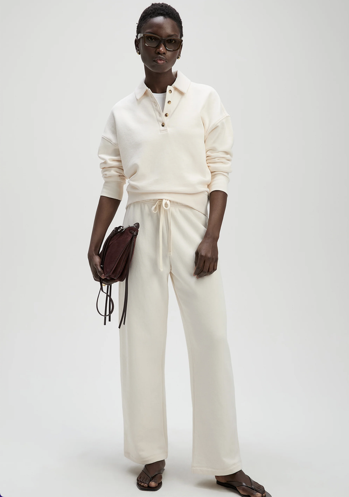 Cream high-waisted French terry sweatpants by Sold Out NYC, styled with dark glasses and burgundy bag.
