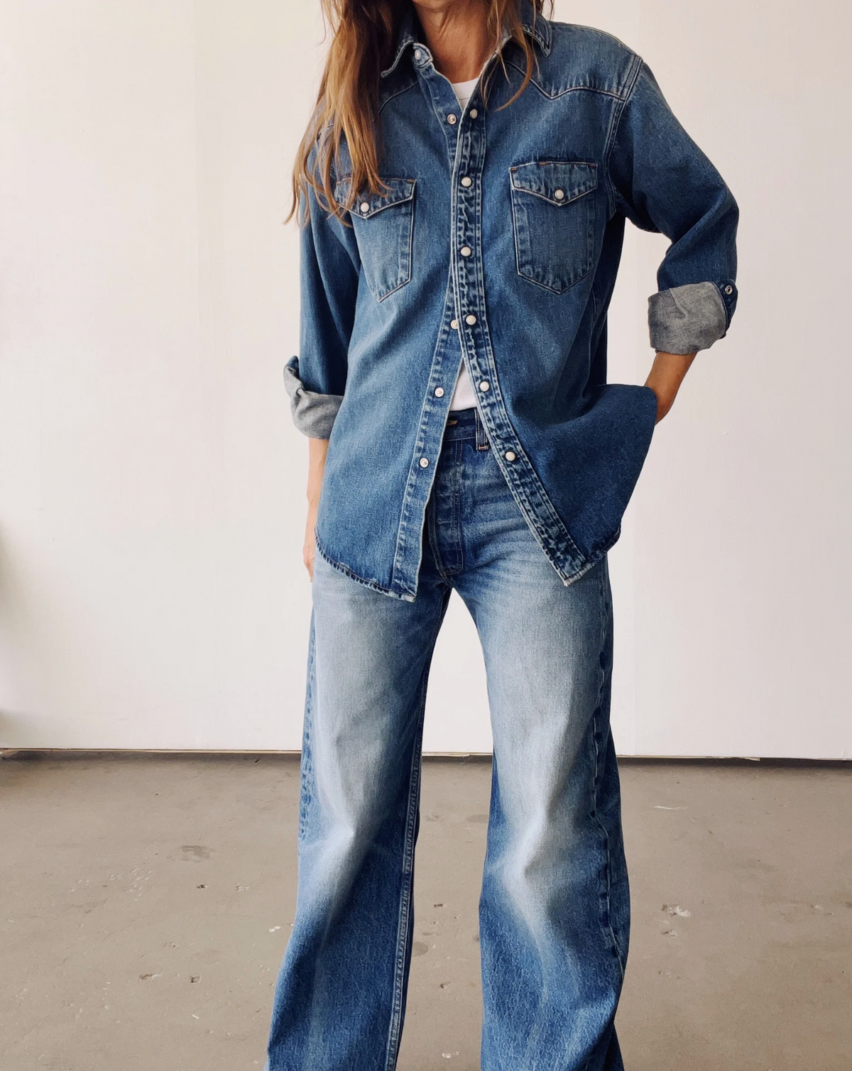 Indoors, someone wears The Western Shirt by Hey Gang with wide-leg blue jeans, creating a casual, relaxed look in Japanese denim with a subtle vintage finish. Sleeves are rolled and the person's face isn't visible.