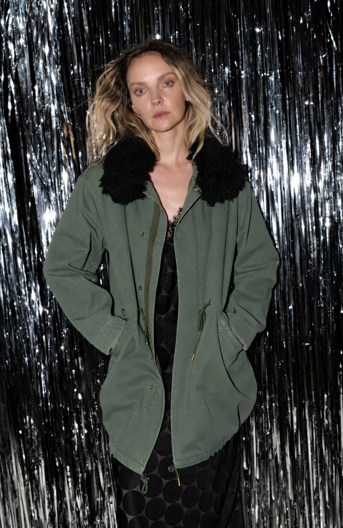 Oversized olive green Le Superbe Utility Anorak with black faux-fur collar, worn over a black dress.