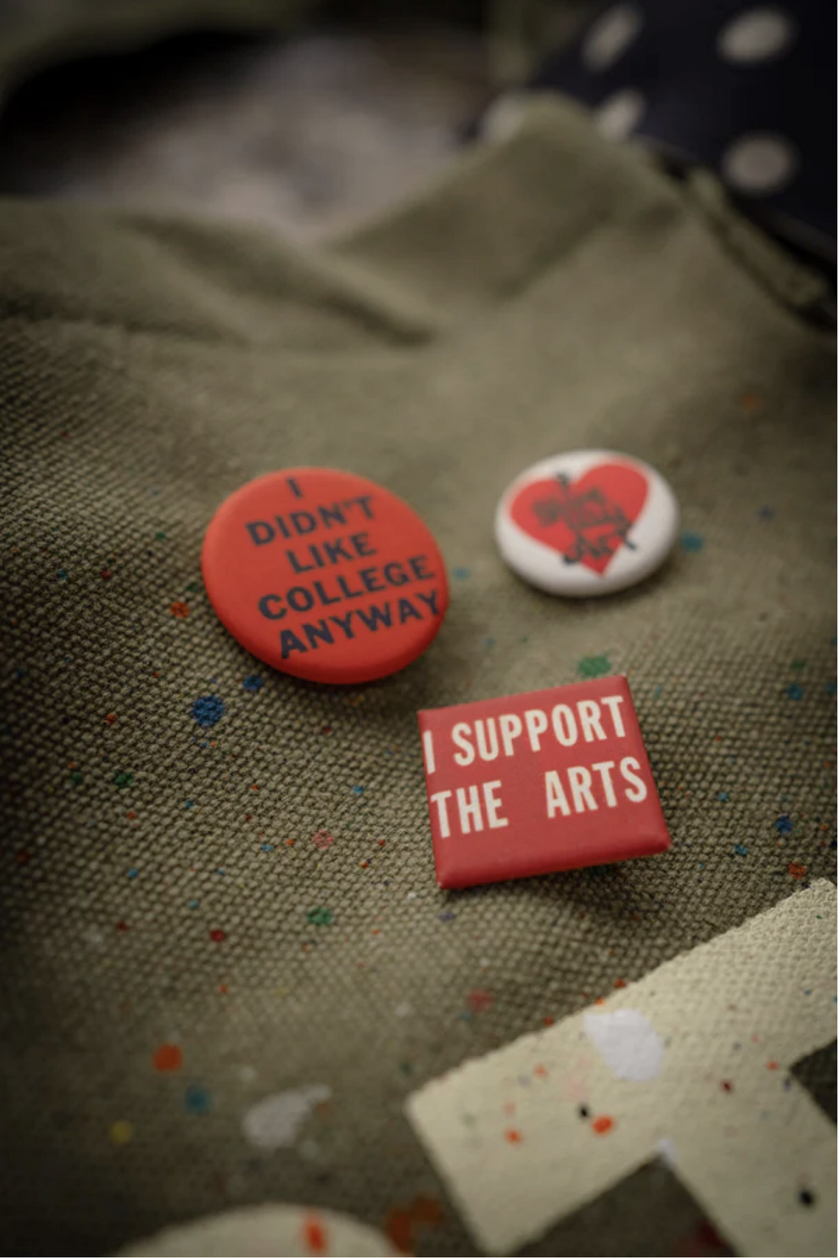 The Artist Tote by Made Worn features three custom buttons on cotton canvas: a red pin with "I DIDN'T LIKE COLLEGE ANYWAY," a small white heart pin, and a square red pin that reads "I SUPPORT THE ARTS.