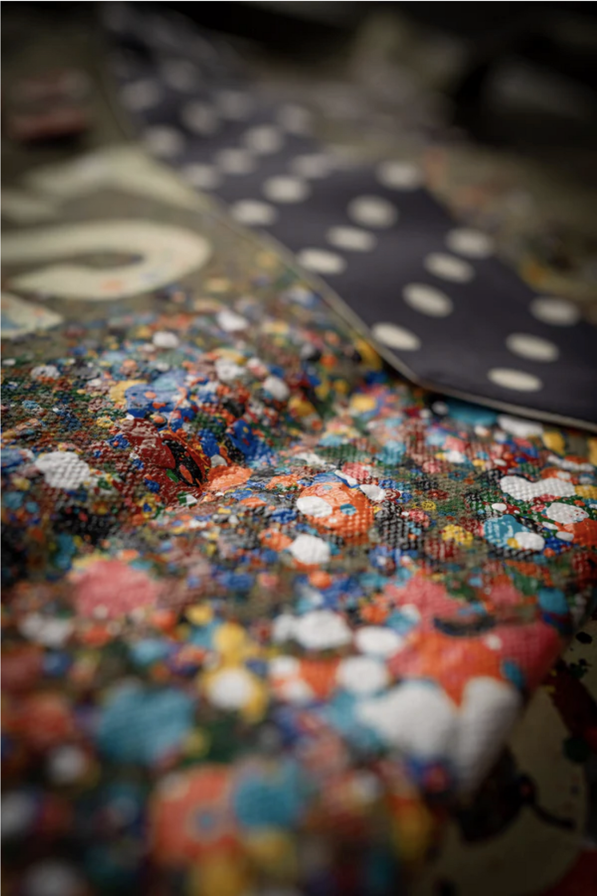 Close-up of colorful cotton canvas fabric with red, blue, orange, and white dots next to a Made Worn Artist Tote featuring a white polka dot pattern. The limited-edition tote appears slightly out of focus in the background.
