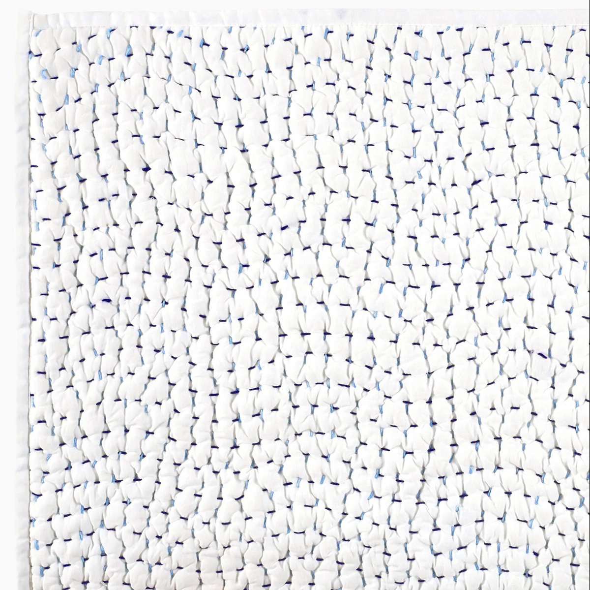 A close-up of the John Robshaw Hand Stitched Coverlet Queen reveals white fabric with a unique, gathered texture and delicate blue stitches, creating an irregular, puckered pattern across its hand-stitched surface.