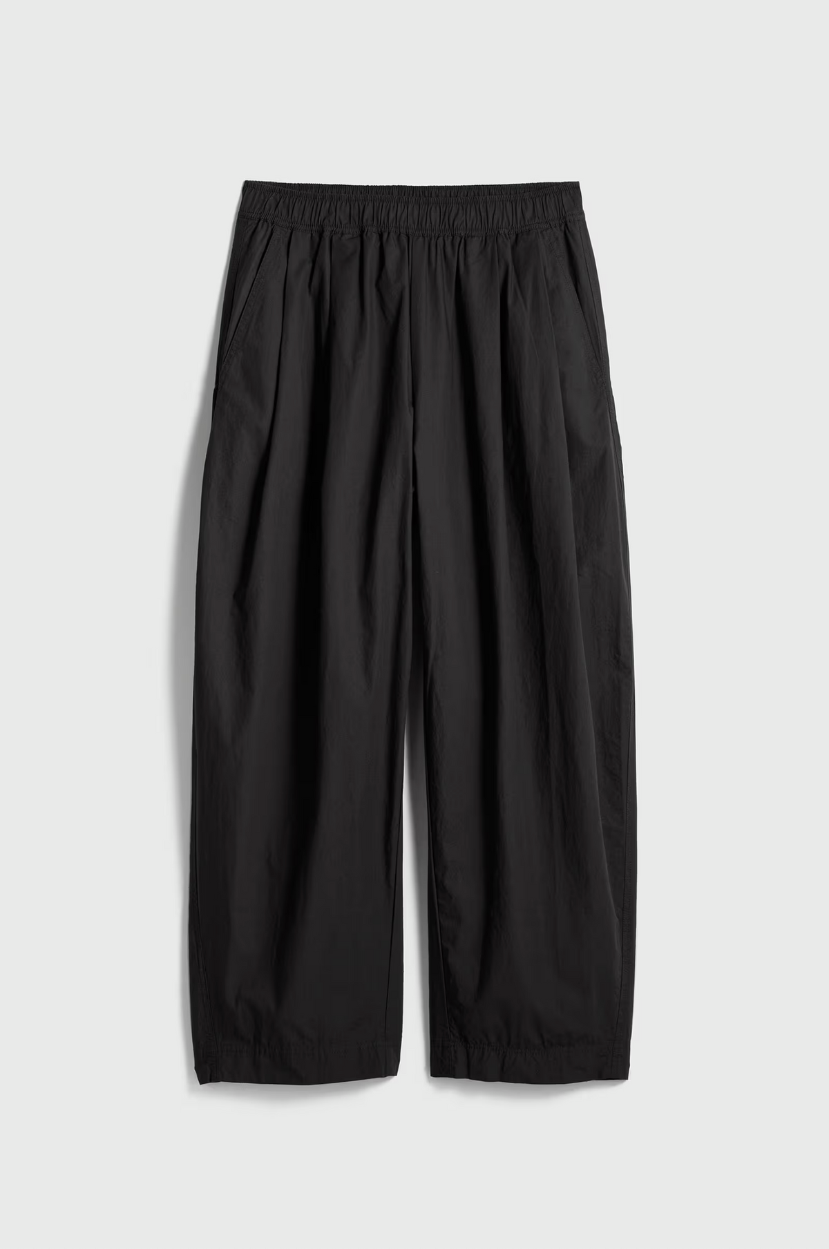 The Apiece Apart Spa Pleat Pant, crafted from black organic cotton, features a wide-leg cut, elastic waistband, and side pockets, shown flat on a light gray background.