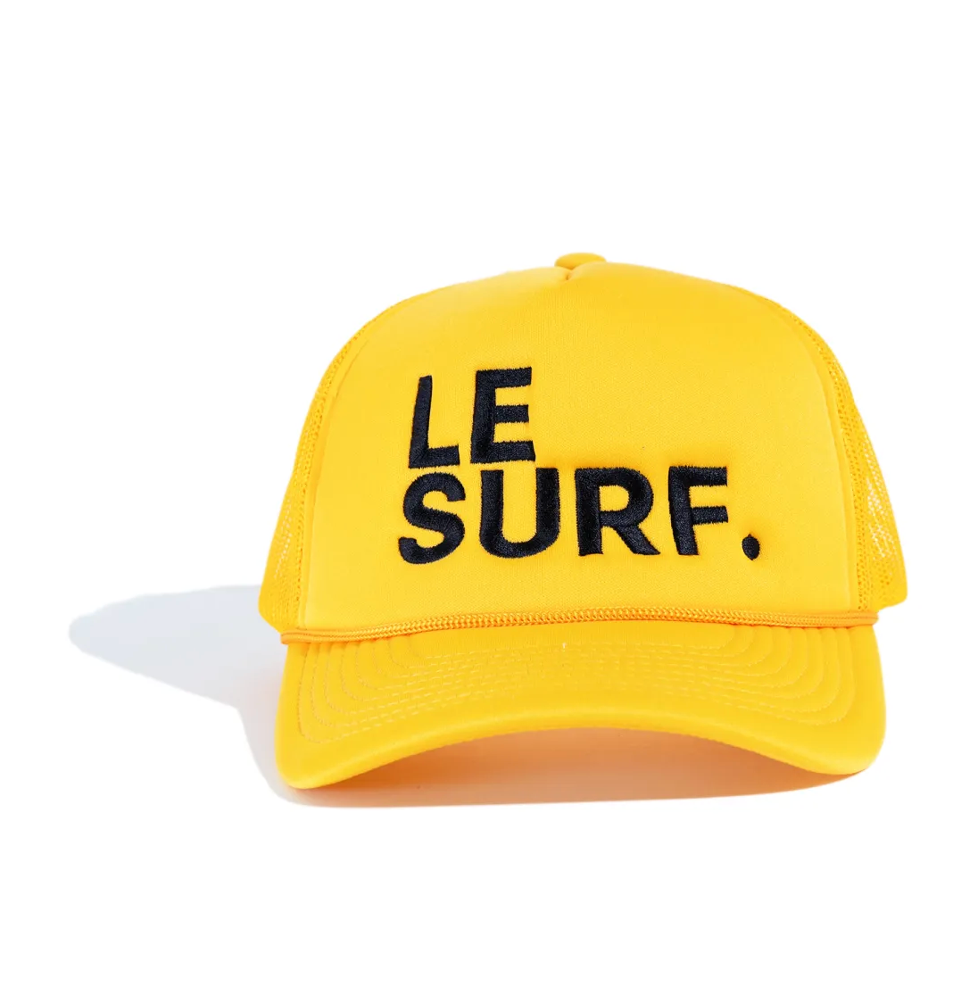 The Le Surf Hat by Ping Pong Surf Club is a bright yellow mesh trucker cap featuring bold black "LE SURF." embroidery on the front, shown against a white background.