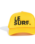 The Le Surf Hat by Ping Pong Surf Club is a bright yellow mesh trucker cap featuring bold black "LE SURF." embroidery on the front, shown against a white background.