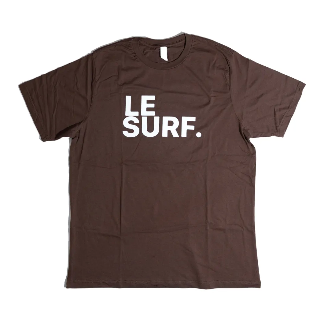 The Le Surf Tee by Ping Pong Surf Club is a brown unisex cotton t-shirt with "LE SURF." printed in bold white letters on the chest, featuring the classic Le Surf logo.