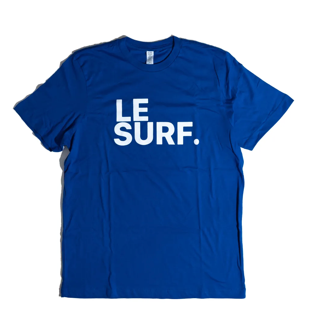 The Le Surf Tee by Ping Pong Surf Club is a royal blue unisex cotton t-shirt with bold white “LE SURF.” text and the classic Le Surf logo, shown on a plain white background.
