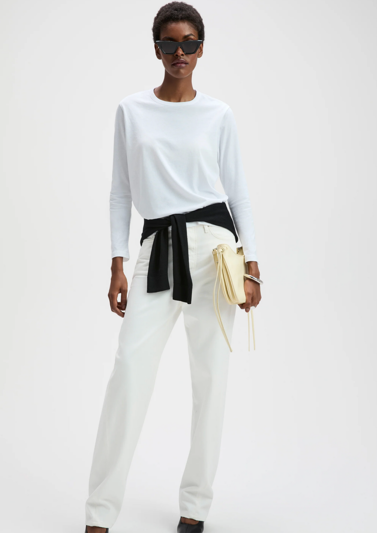 White long sleeve tee by Sold Out NYC styled with a black sweater at the waist and yellow handbag, modern street look.