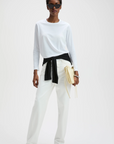 White long sleeve tee by Sold Out NYC styled with a black sweater at the waist and yellow handbag, modern street look.
