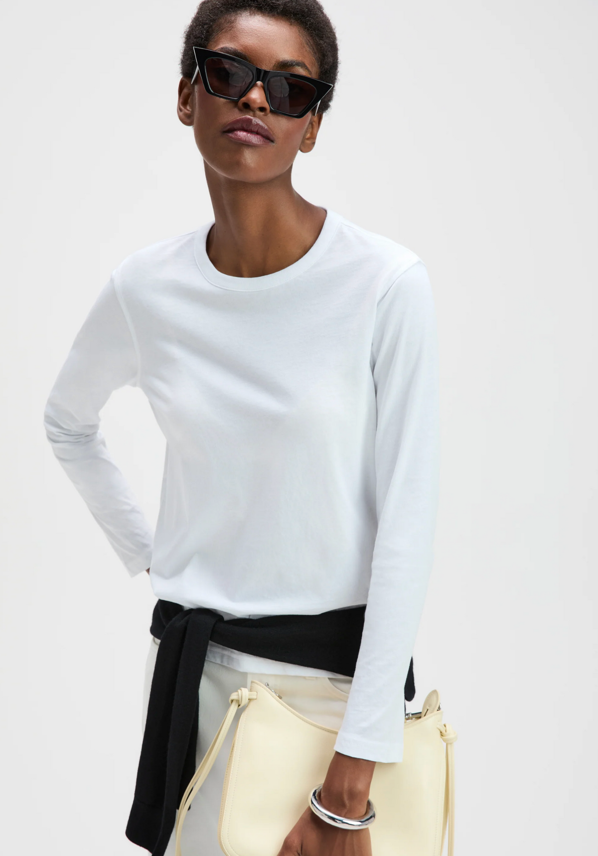 Long sleeve Perfect Tee by Sold Out NYC styled with sunglasses, cream bag, and black sweater at the waist.