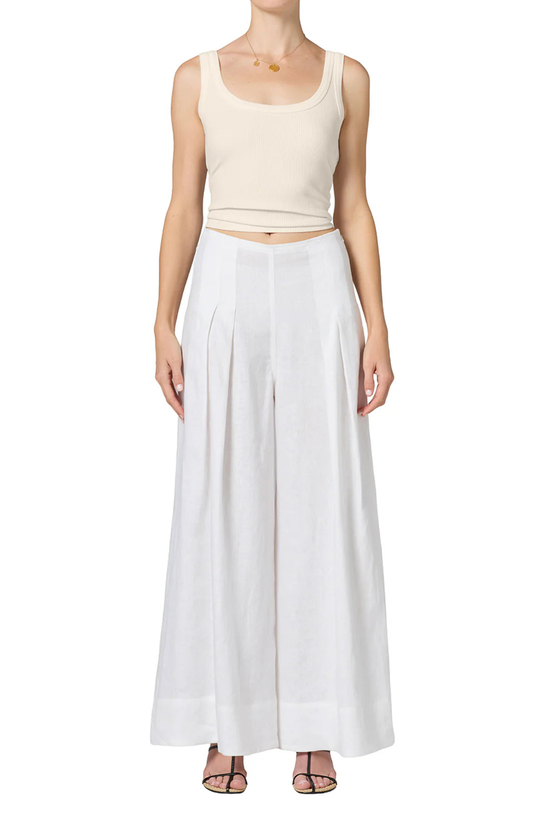 A person wears the nova tank by Citizens Of Humanity/AGOLDE, a fitted ribbed scoop-neck top, with high-waisted white pleated wide-leg pants and black strappy sandals, standing facing forward against a white background.