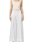 A person wears the nova tank by Citizens Of Humanity/AGOLDE, a fitted ribbed scoop-neck top, with high-waisted white pleated wide-leg pants and black strappy sandals, standing facing forward against a white background.