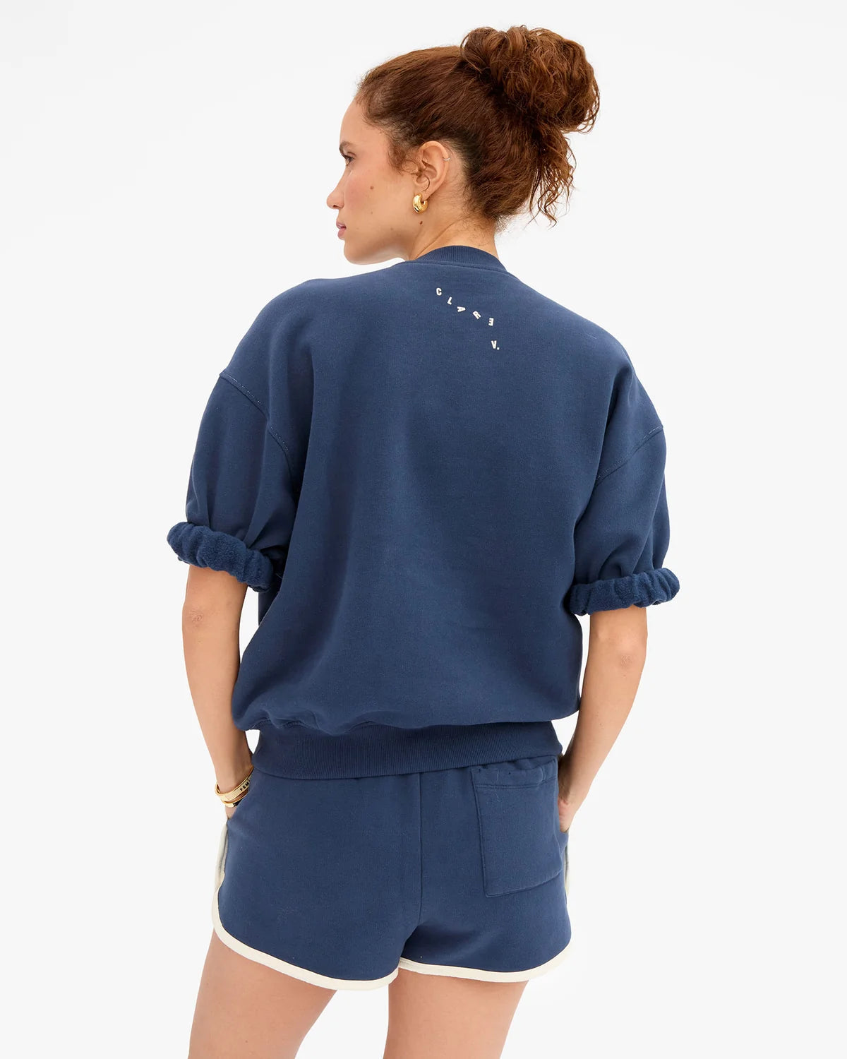 Blue cotton Clare Vivier Le Jogging Shorts with side seam pockets, modeled from the back by a woman with curly hair.