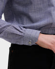 A person wears the Denim Country Club shirt by Sarah Alexandra, LLC—a tailored-fit blue chambray with a one-piece collar—paired with black pants, hand in pocket and a cuff button visible.