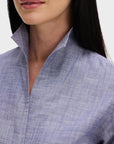 A woman with long dark hair models Sarah Alexandra, LLC’s Denim Country Club shirt, showing its tailored fit and high, stiff one-piece collar turned up. Only her lower face and upper torso are visible.