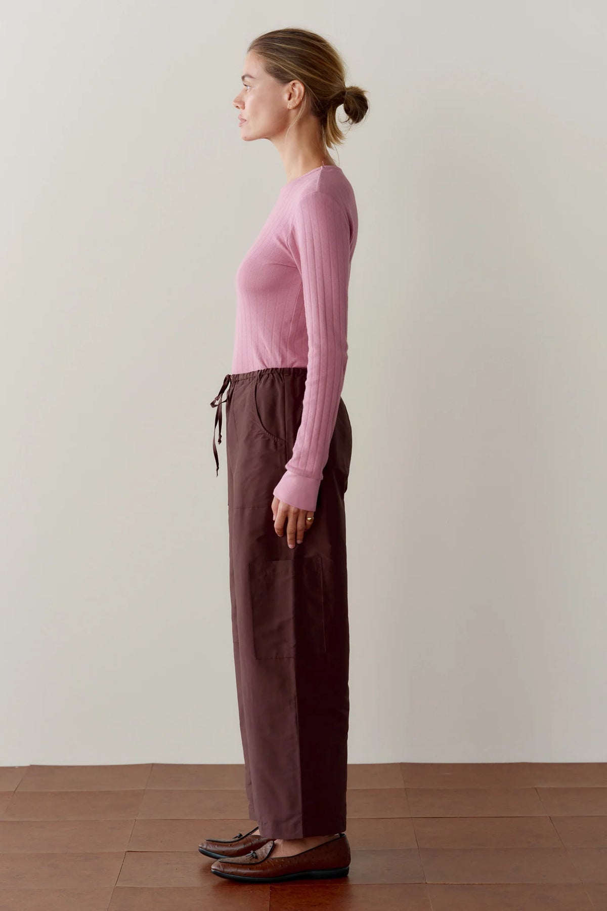 Donni The Taffeta Drawstring Cargo Pant in brown paired with a cropped pink ribbed long-sleeve shirt.