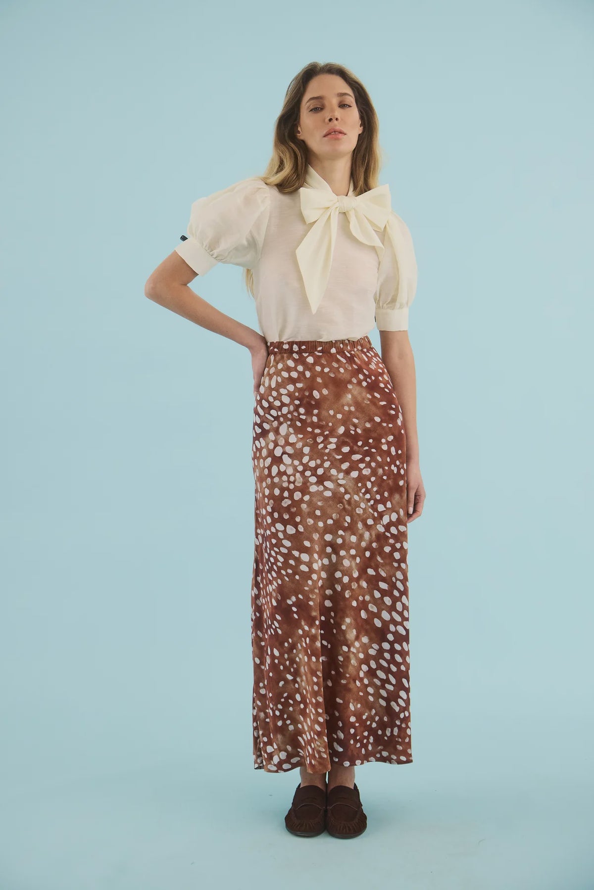 Hunter Bell NYC Suki Skirt in white, styled with a blouse, modeled against a light blue background.
