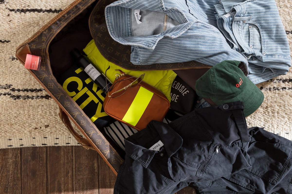 Open suitcase with colorful travel essentials on a patterned rug, styled for a relaxed Bungalow getaway.