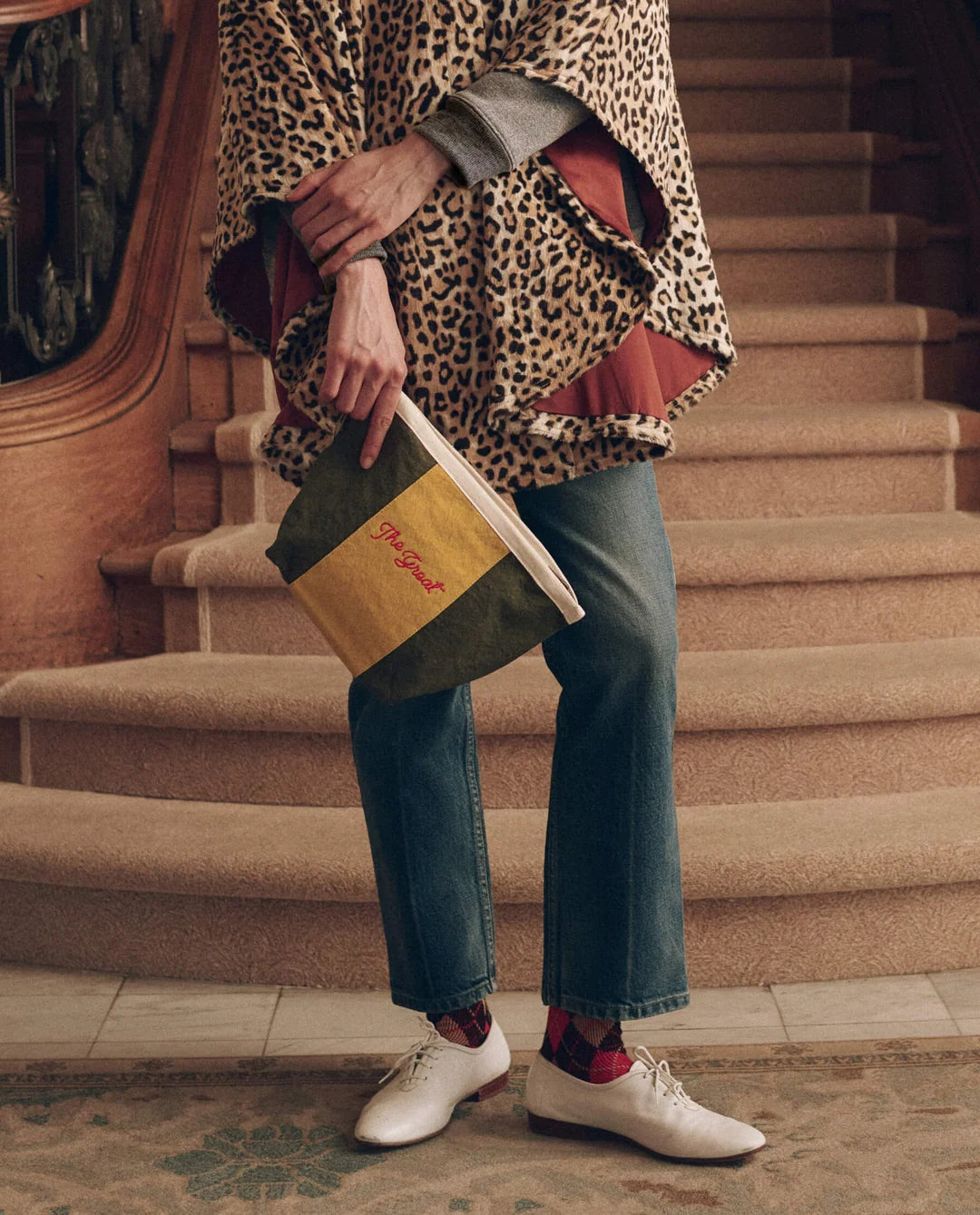 The Striped Pouch in green and yellow cotton canvas held by a person in a leopard print poncho and jeans.