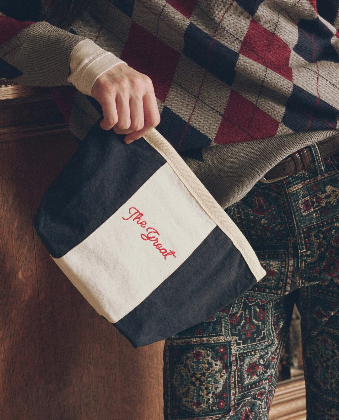 The Striped Pouch in black and white cotton canvas with red embroidery, held by a person.