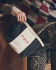 The Striped Pouch in black and white cotton canvas with red embroidery, held by a person.