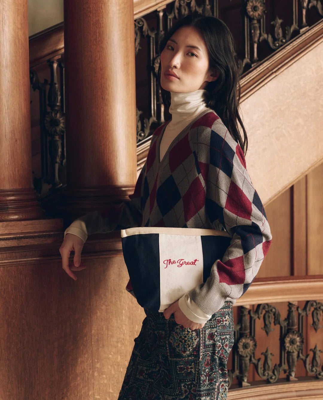 The Striped Pouch in navy and white cotton canvas with red embroidery, held by a woman in an argyle sweater.
