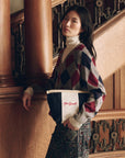 The Striped Pouch in navy and white cotton canvas with red embroidery, held by a woman in an argyle sweater.