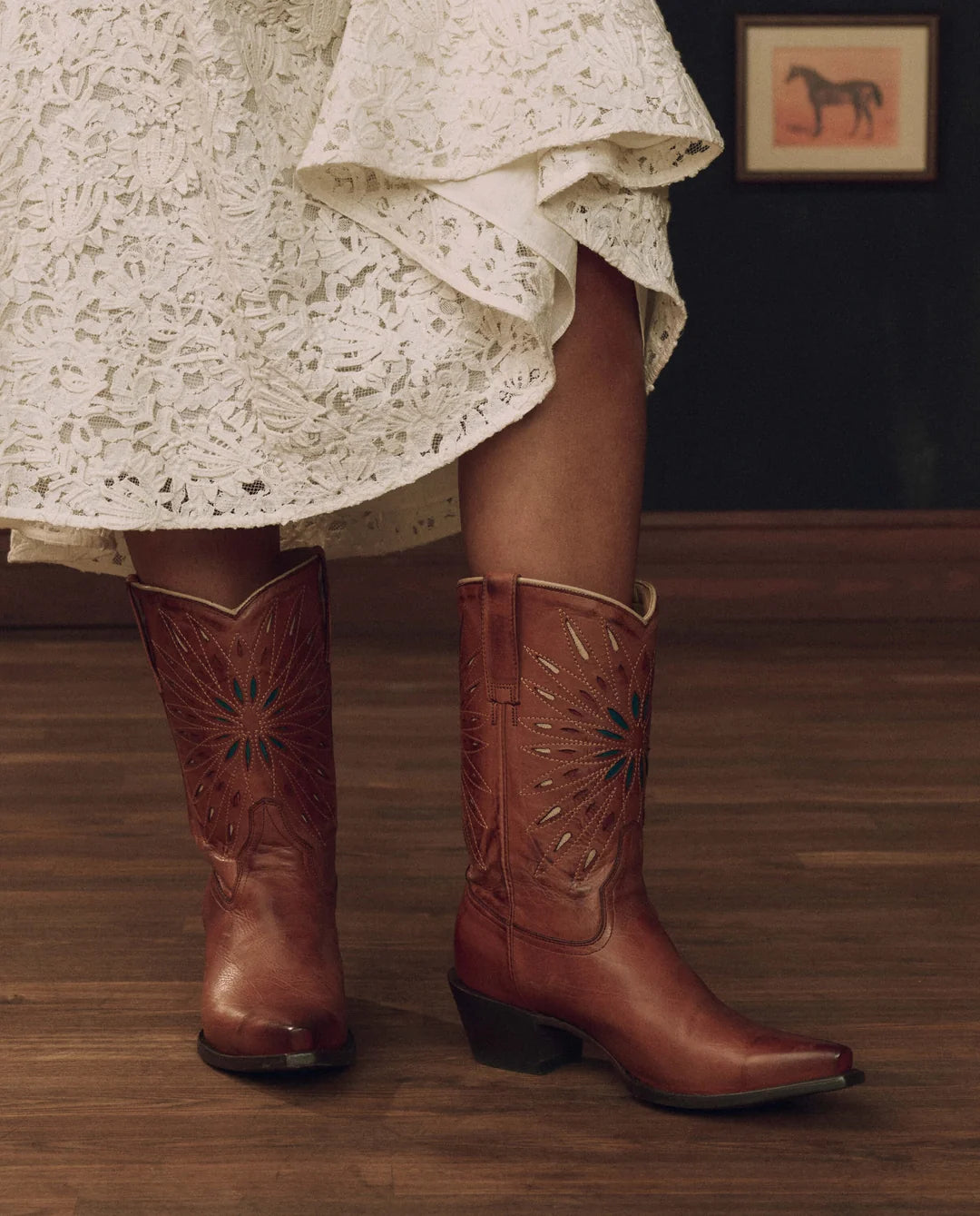 The Great Inc. Southwest Cowboy Boot in white lace paired with a rustic wood floor and horse art backdrop.
