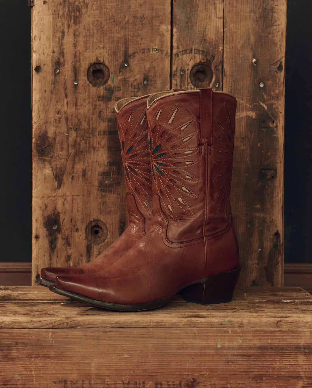 Handcrafted leather cowboy boot with decorative stitching by The Great Inc., displayed on rustic wood.