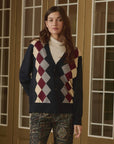 The Argyle Menswear Cardigan in navy, burgundy, and cream worn over a beige mock neck top.