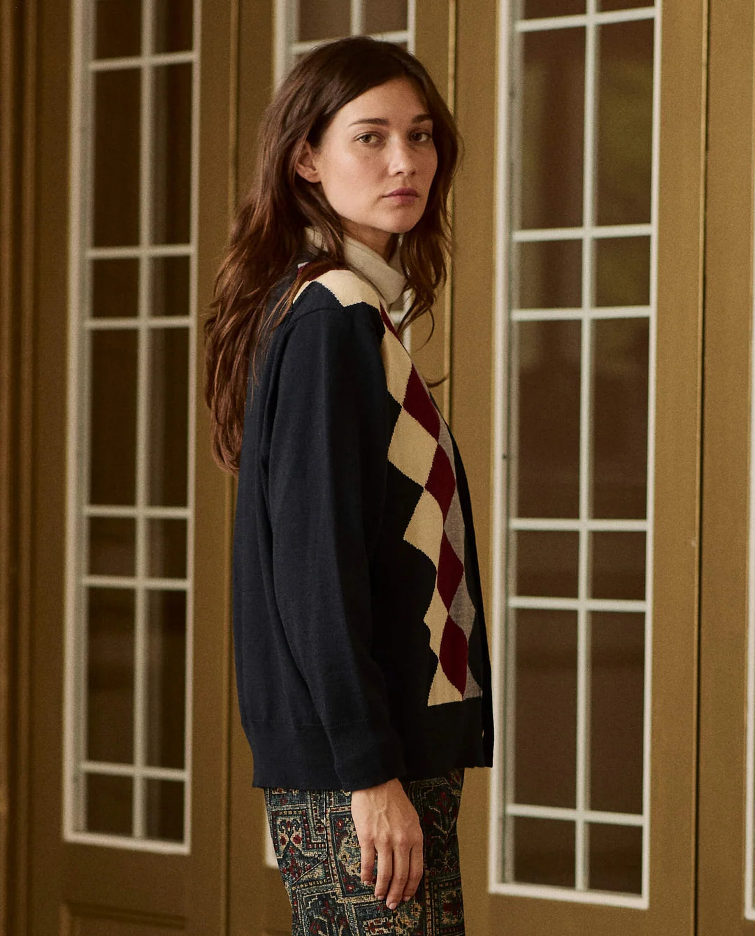 Argyle cardigan in dark blue, red, and beige over a cream turtleneck by The Great Inc.