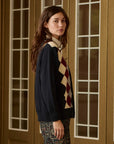 Argyle cardigan in dark blue, red, and beige over a cream turtleneck by The Great Inc.
