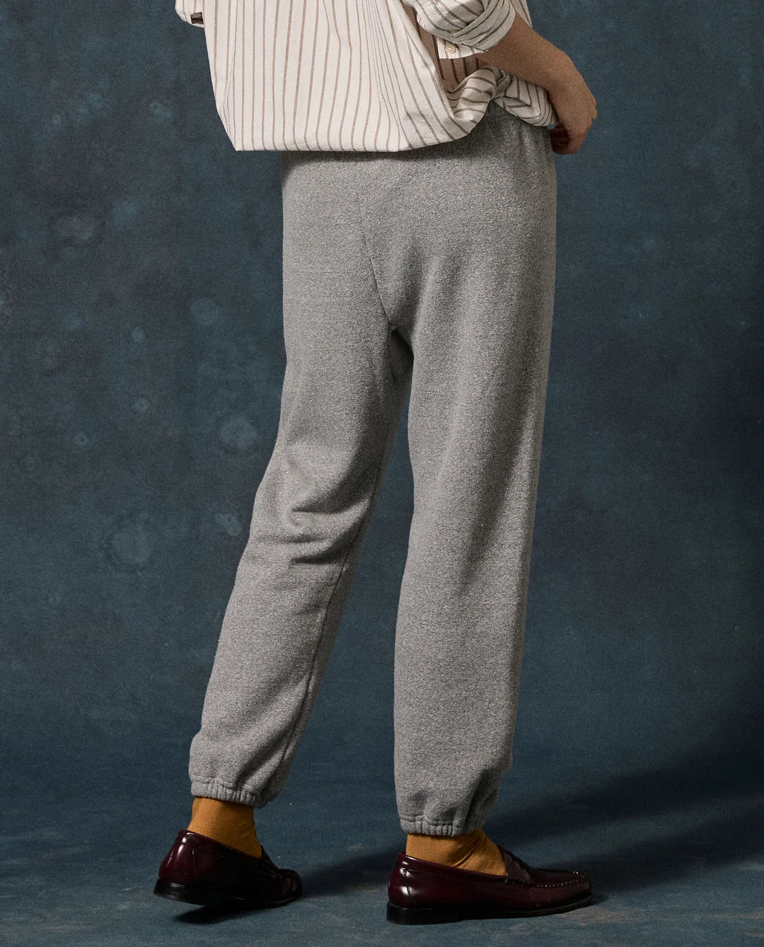 Heather grey The Fleece Stadium Sweatpants with elasticized cuffs paired with burgundy loafers, back view.