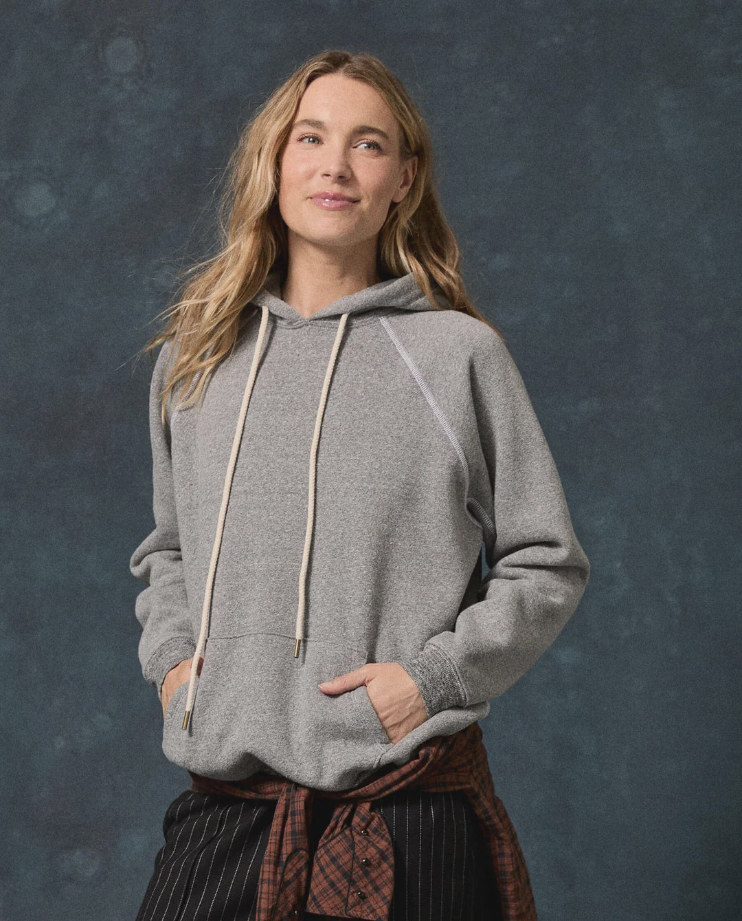 The Fleece Pullover Hoodie in vintage grey French Terry with drawstring and front pocket, worn by a woman.